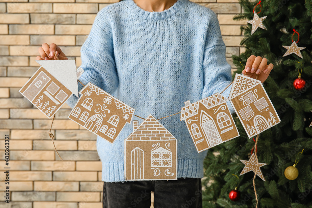 Woman holding rope with handmade Christmas garland on brick background