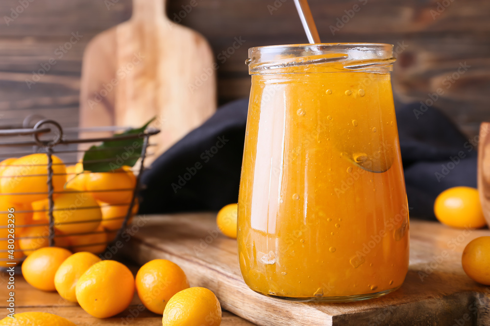 Jar of tasty kumquat jam and fresh fruits on wooden background