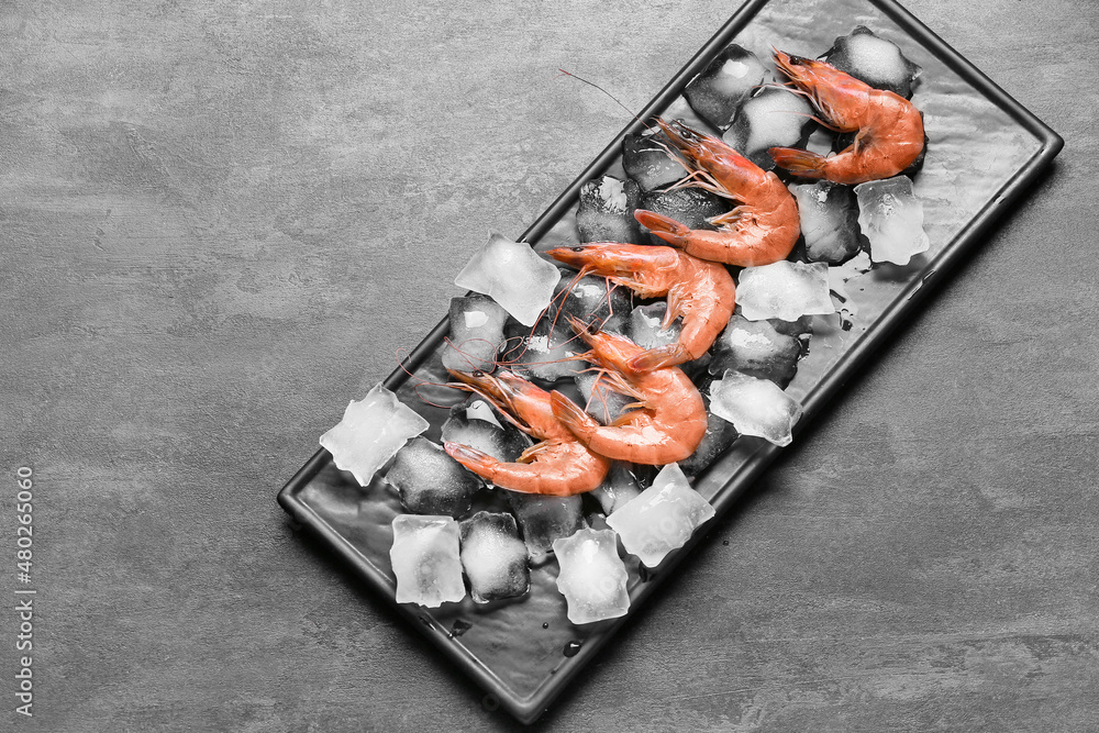 Board with uncooked shrimps and ice cubes on black background