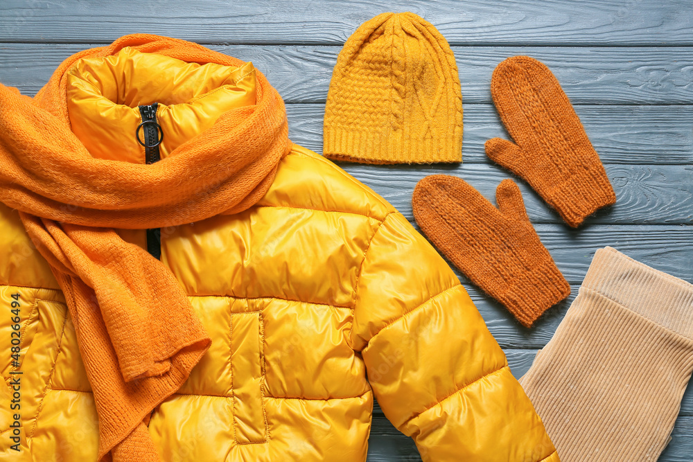 Stylish jacket, hat, scarf and mittens on grey wooden background