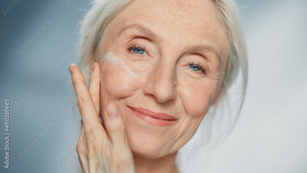 Portrait of Beautiful Senior Woman Gently Applying Face Cream. Elderly Lady Makes Her Skin Soft, Smo