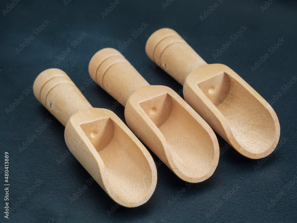 Three empty wooden scoops for bulk products on a dark background. Close-up.