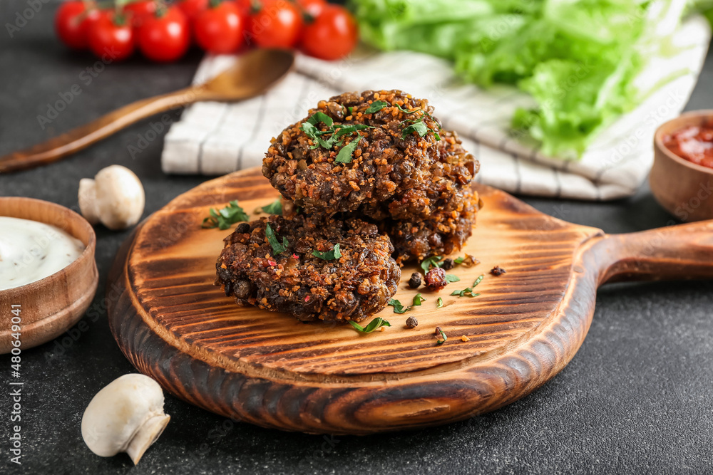 Board with tasty lentil cutlets on dark background