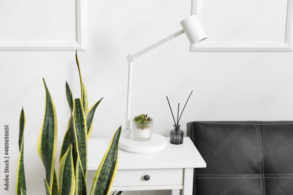 White lamp, flowerpot and reed diffuser on table near light wall