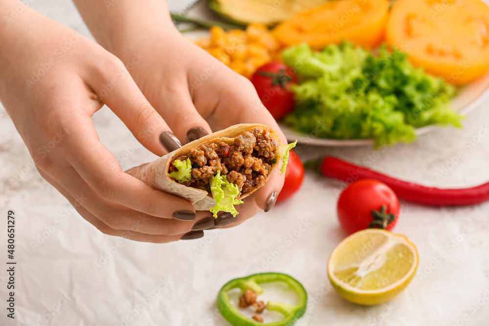 Woman holding tasty burrito on light background