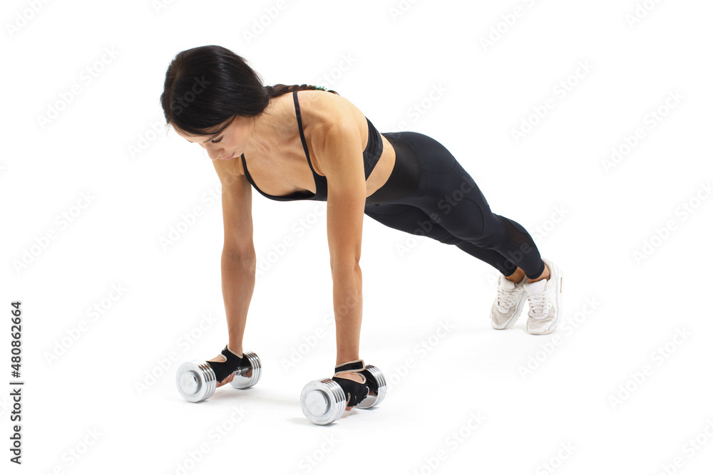 muscular woman in black sportswear doing plank exercise with dumbbells isolated on white background