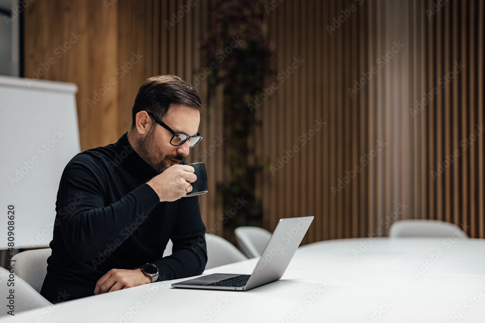 Adult company manager, taking a sip of his warm tea, while working.