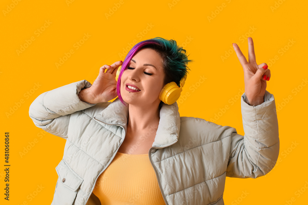 Beautiful woman with unusual hair listening to music on yellow background