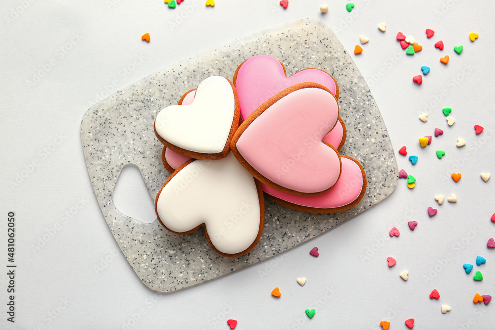 Board with tasty heart shaped cookies on light background