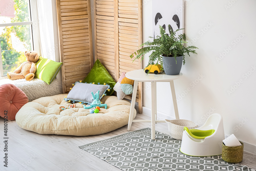 Potty and basket with toilet paper roll near light wall in child room