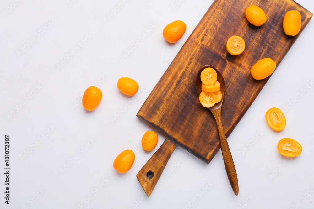 Spoon with tasty kumquat fruits on light background