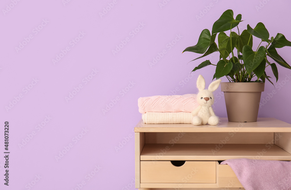 Houseplant, sweaters and toy rabbit on table near color wall