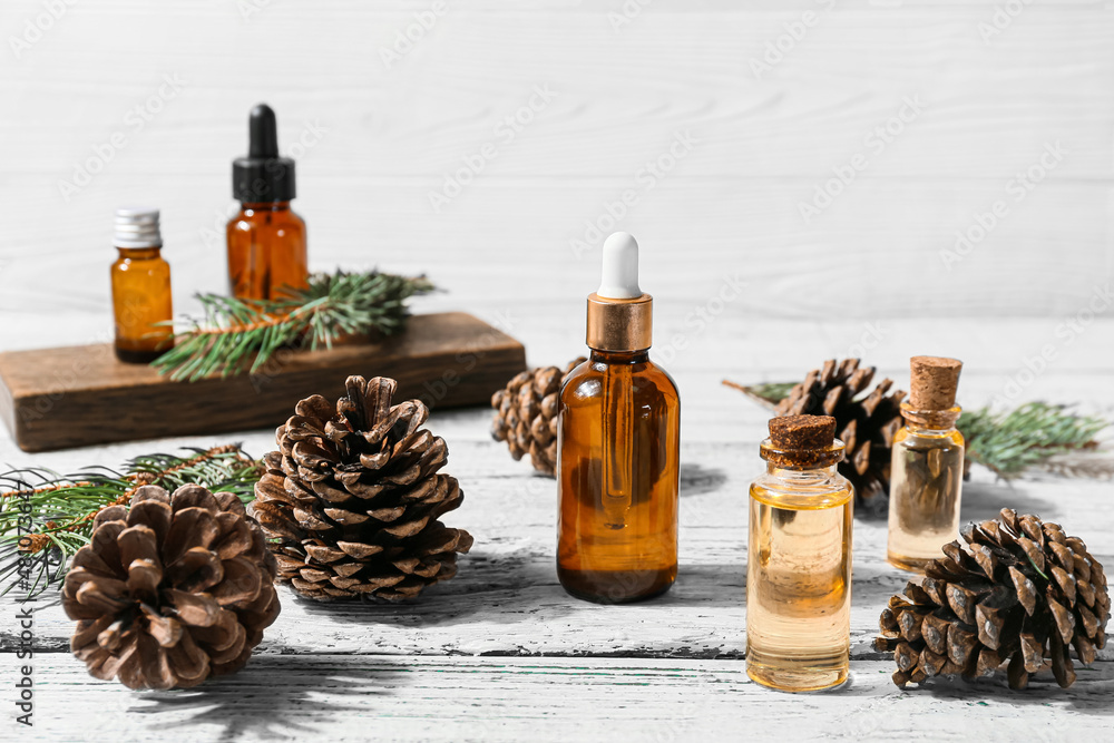 Bottles of essential oil and pine cones on light wooden background