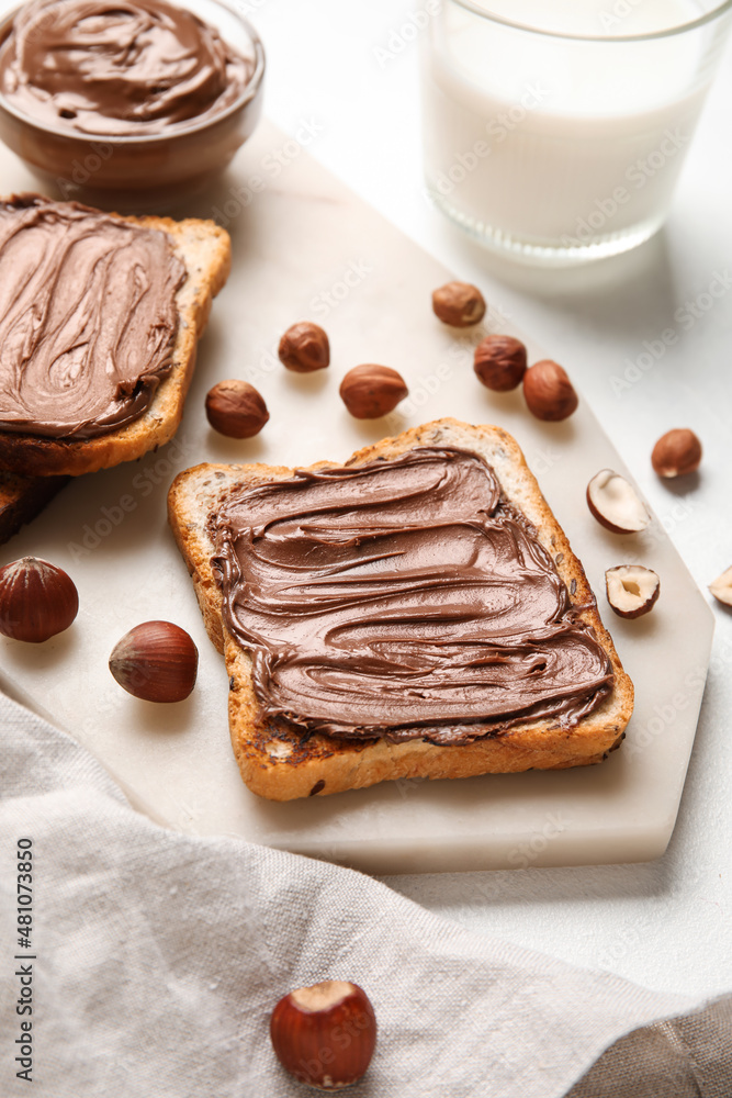 Board of bread with chocolate paste and hazelnuts on white background