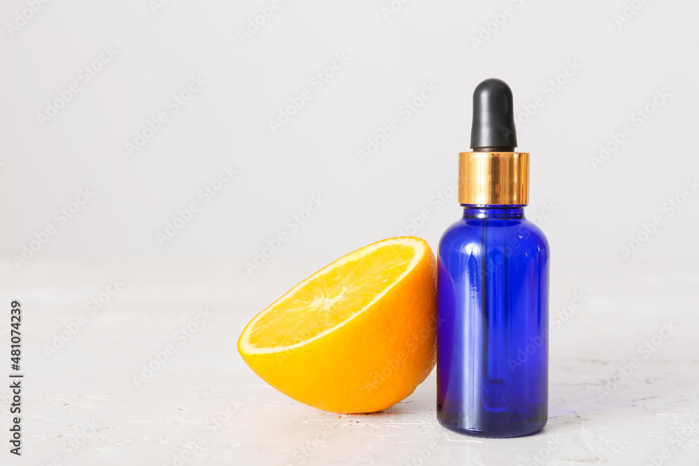 Bottle of essential oil and fresh orange on light background, closeup