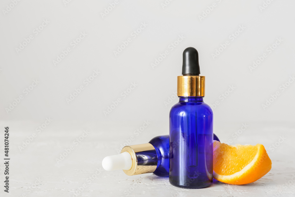 Bottles of essential oil and fresh orange on light background, closeup