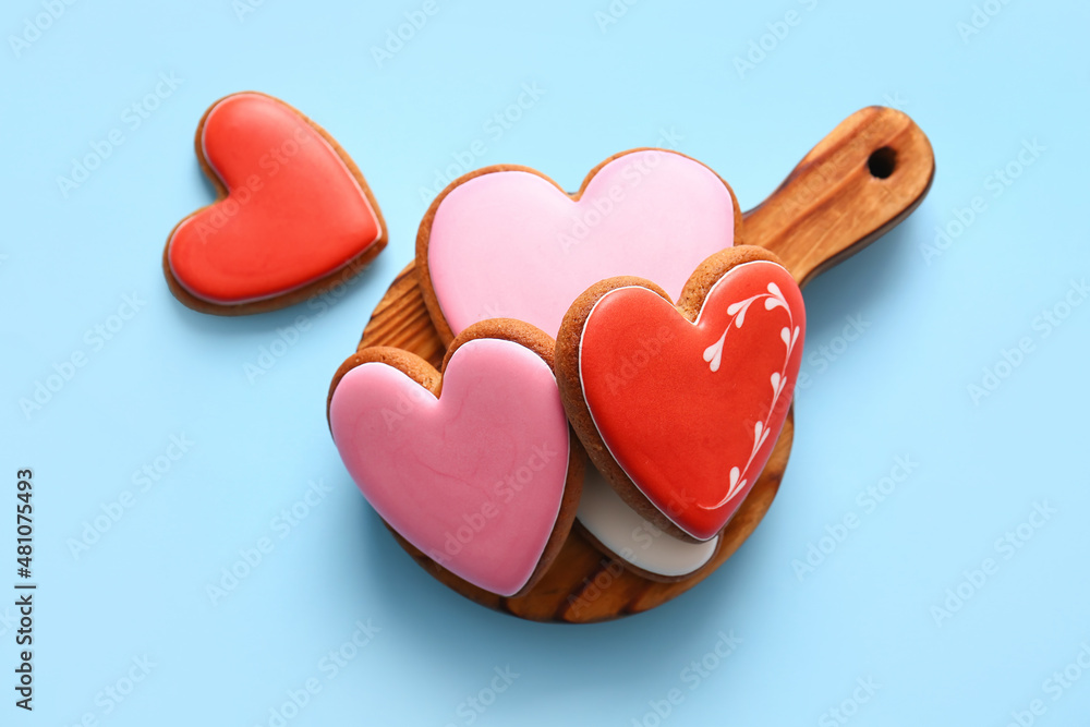 Wooden board with tasty heart shaped cookies on blue background