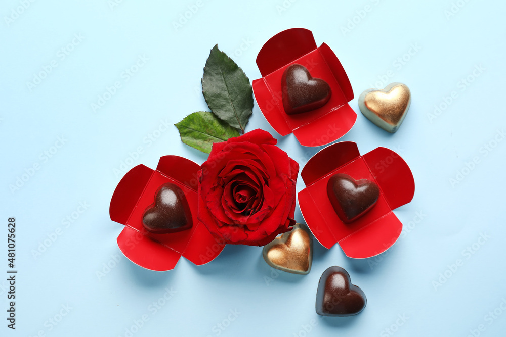 Tasty heart-shaped candies and rose on blue background