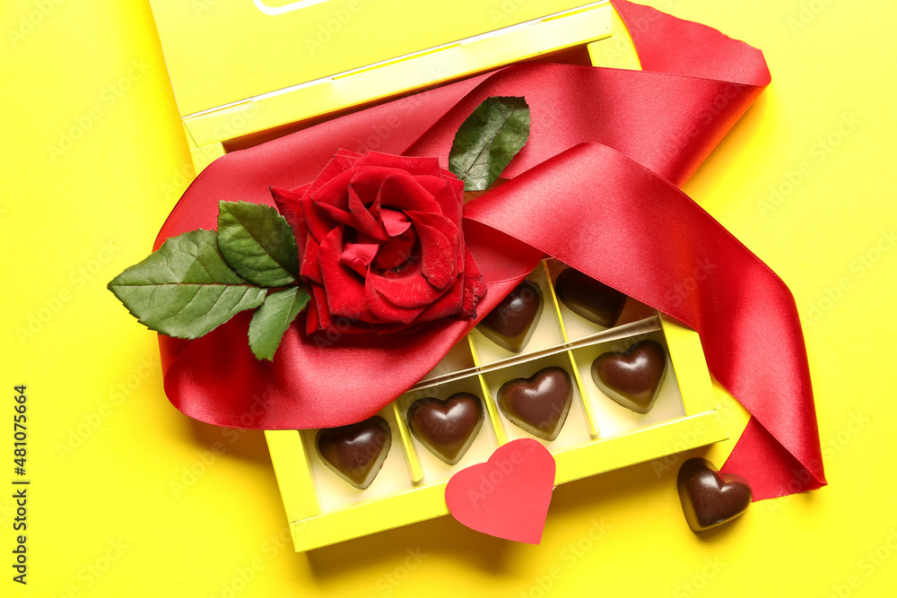 Box with tasty heart-shaped candies and rose on yellow background