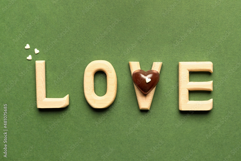 Word LOVE and tasty heart-shaped candy on green background