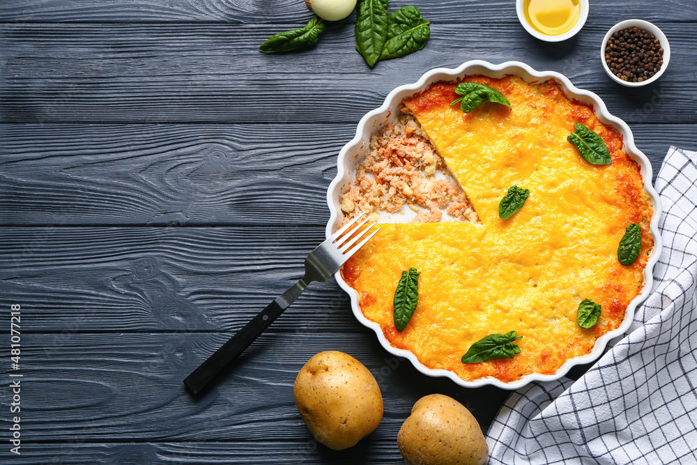 Baking dish with tasty English fish pie on black wooden background