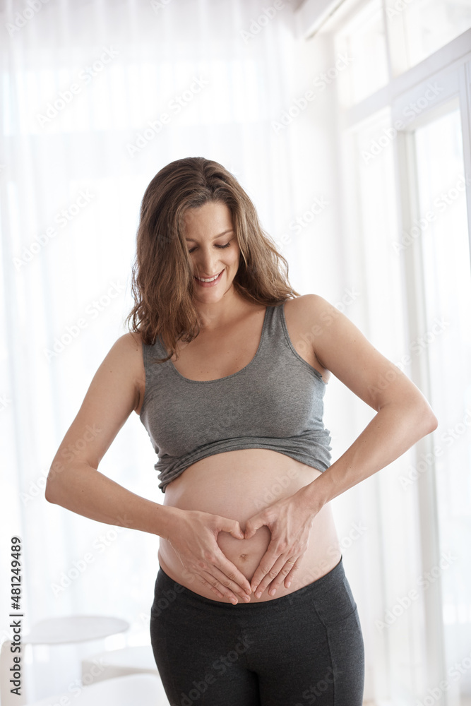 Waiting for the arrival. Cropped shot of a young pregnant woman standing in her home.