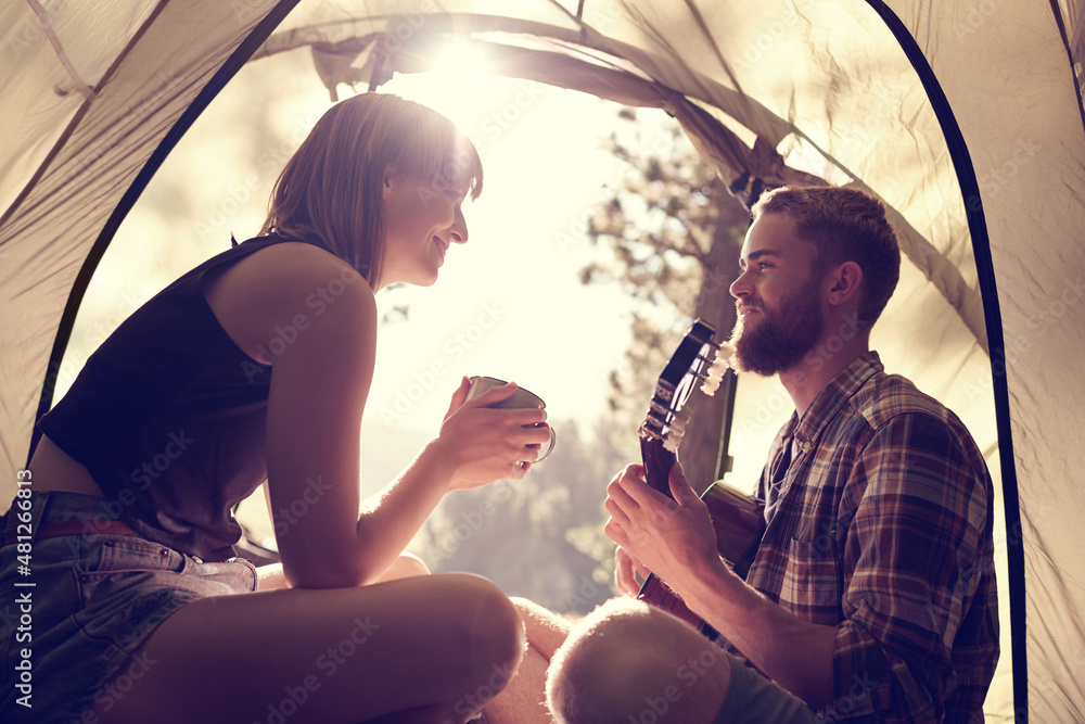 Isnt this the a perfect day. Shot of a young man playing guitar to his girlfriend in a tent.