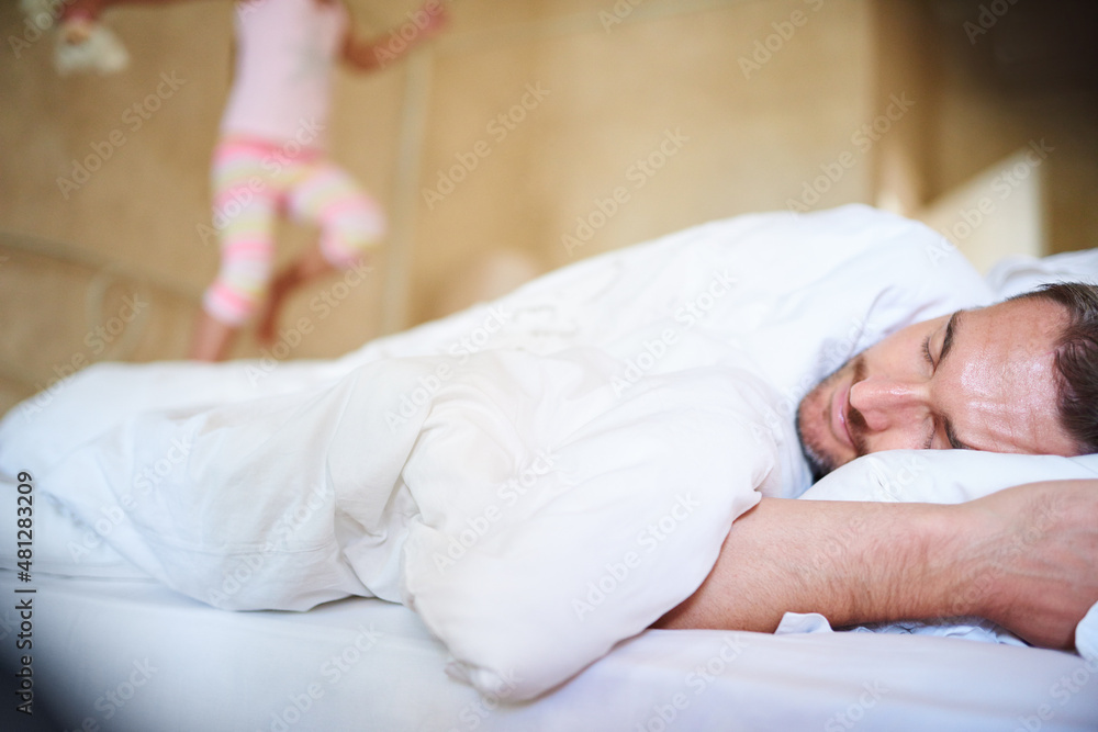 Its morning daddy. Shot of a sleeping dad with his little daughter jumping on the end of the bed.