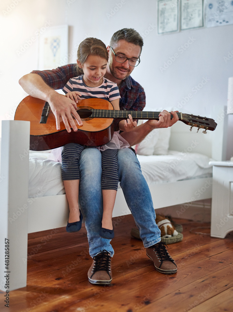 They have a lot in common. Shot of a little girl playing the guitar with her father.