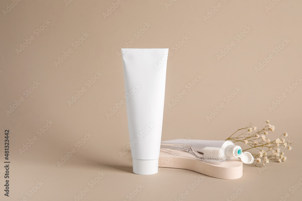 Composition with toothpaste tubes, toothbrush and flowers on beige background