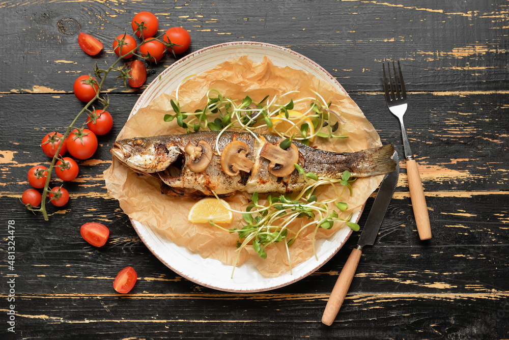 Plate with delicious sea bass fish, vegetables and tomatoes on dark wooden background