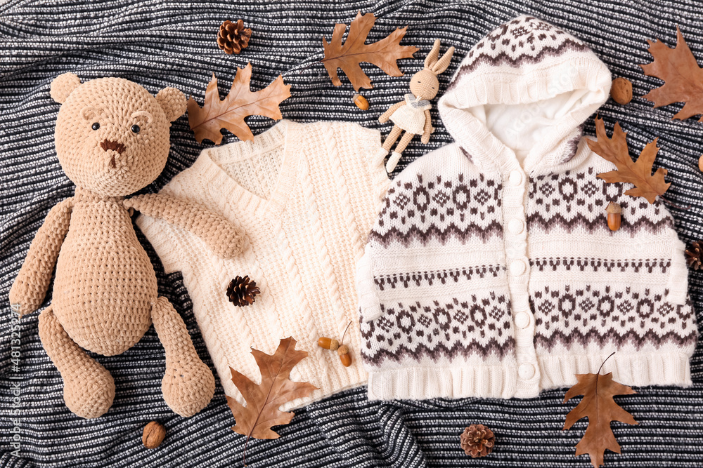 Warm baby clothes, toys and autumn decor on dark fabric background