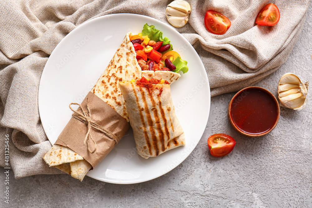 Plate with delicious burritos and sauce on grey background