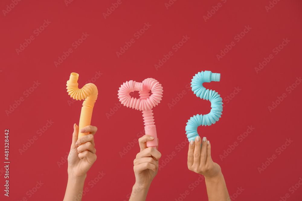 Hands with popular pop tubes on color background