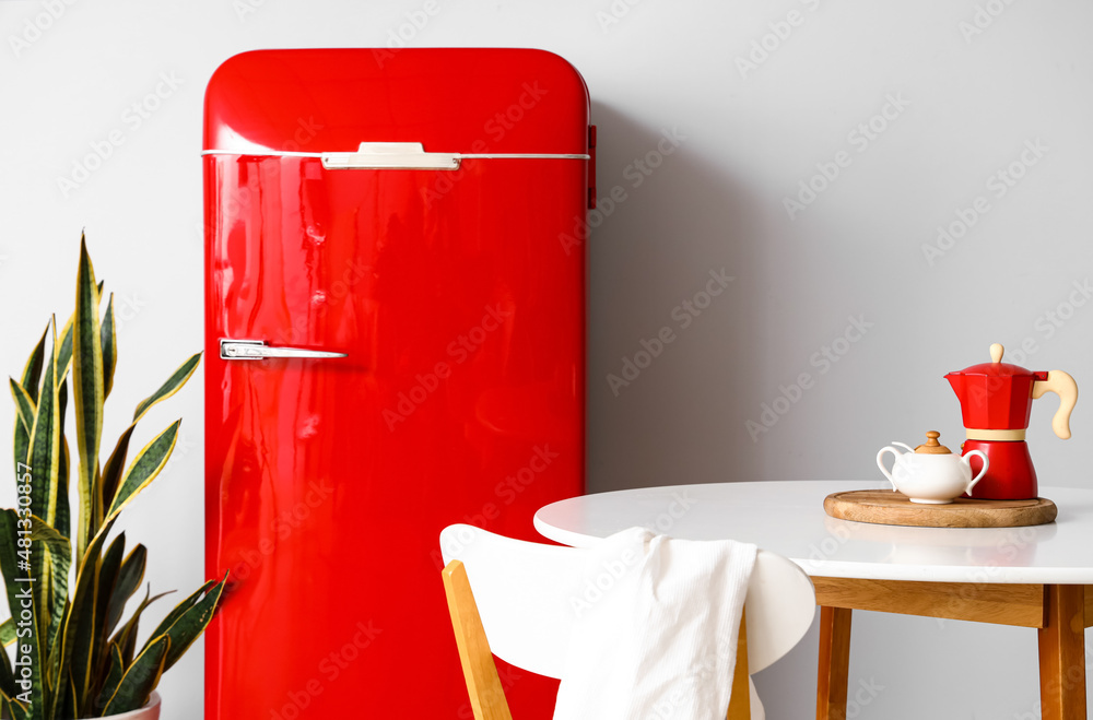 Dining table, red fridge and houseplant near light wall