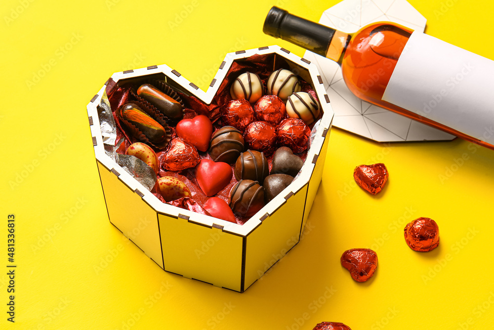 Heart shaped box with tasty chocolate candies on yellow background