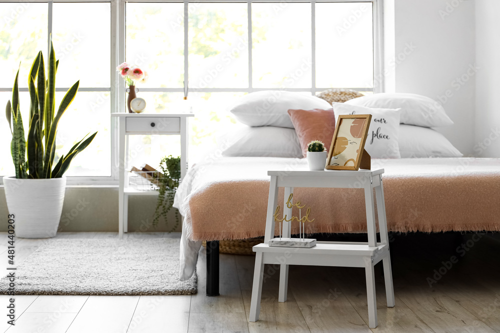 Stylish light bedroom with wooden bedside table near window