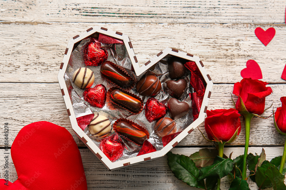 Heart shaped box with tasty chocolate candies and roses on white wooden background