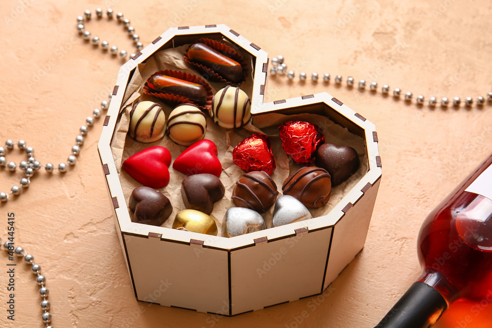 Heart shaped box with tasty chocolate candies on beige background