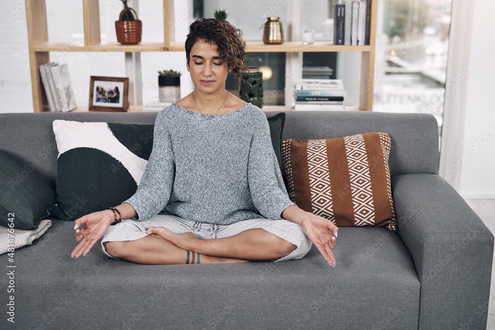 Its about mastering yourself. Shot of an attractive young woman meditating on a sofa at home.