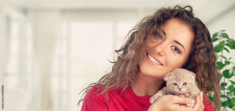 Happy beautiful cheerful young woman with a cute gray cat in her arms at home