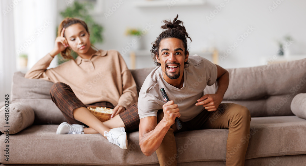 Young african american family couple disagree on tv channel choice while sitting on sofa at home