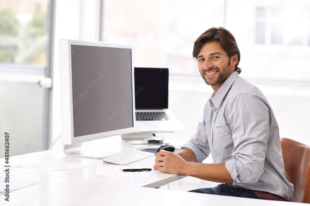 This is easy. A young businessman sitting at his desk and smiling at the camera.