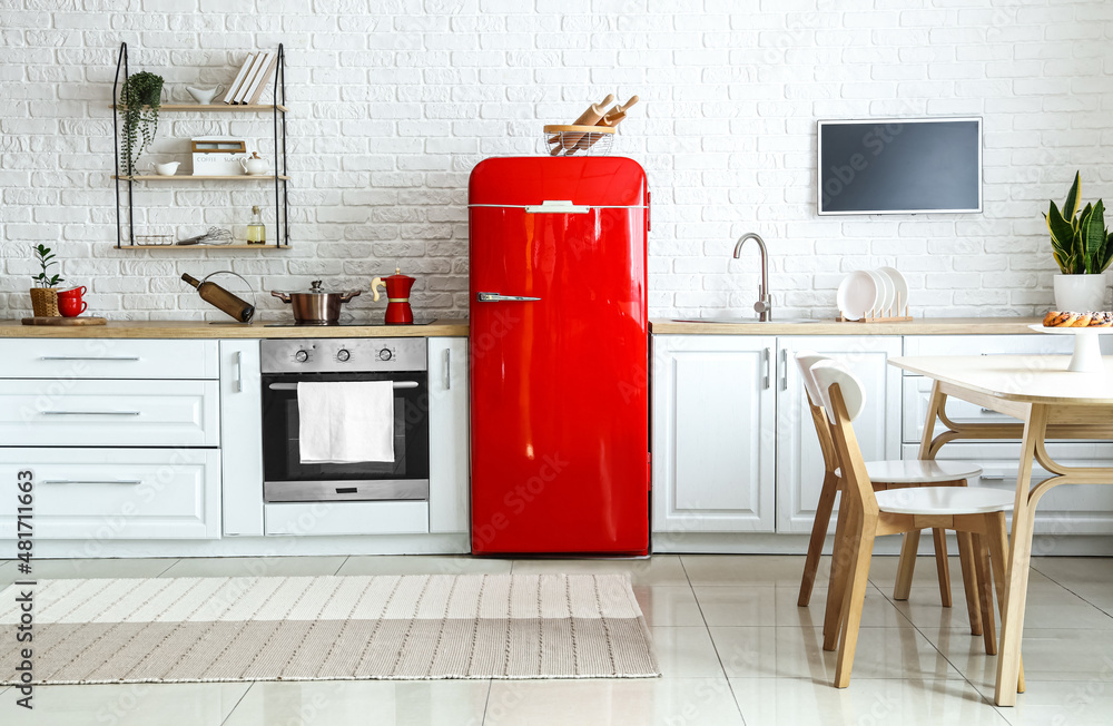 Interior of light kitchen with red fridge, white counters and dining table