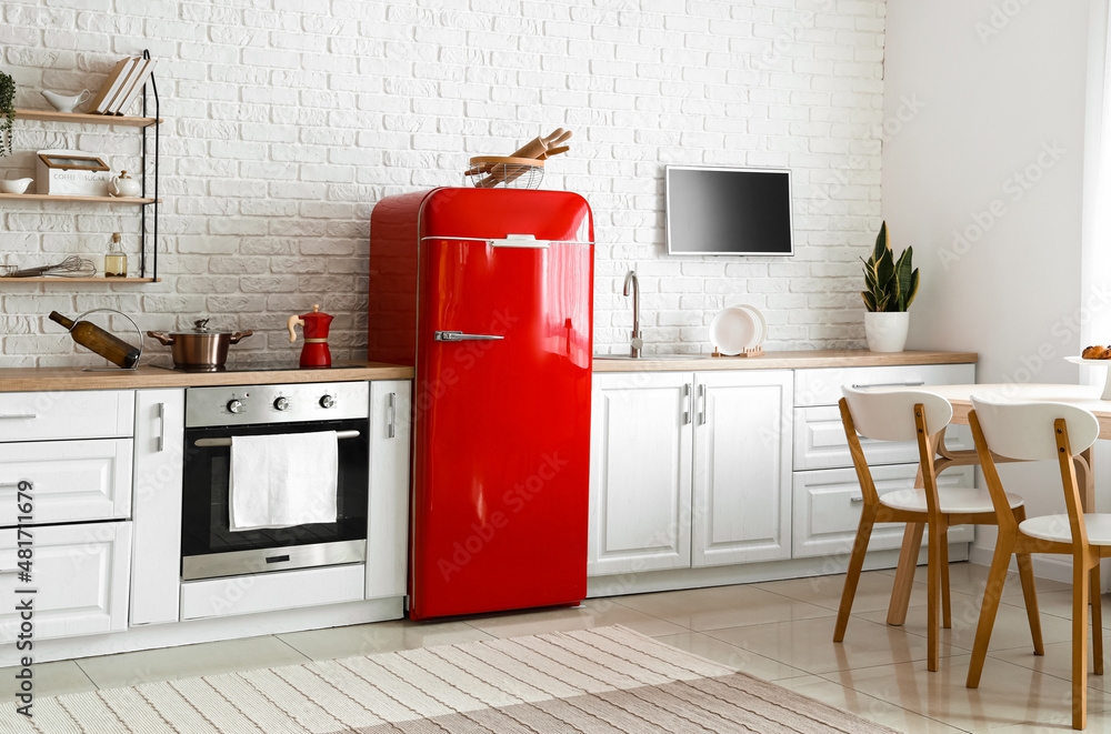 Interior of light kitchen with red fridge, white counters and dining table