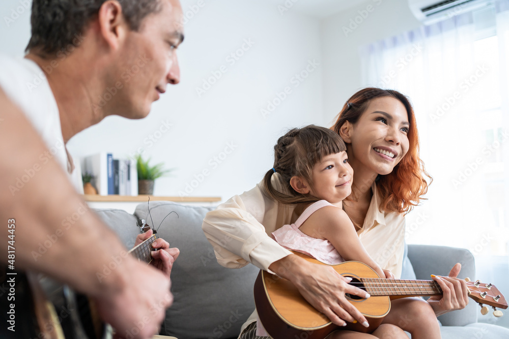 Asian young couple playing guitar with young baby kid together at home. 