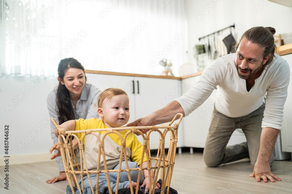 Caucasian loving parents play with baby toddler in kitchen on floor. 