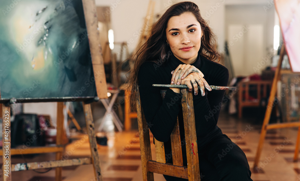 Young female artist looking at the camera while sitting in her art workshop