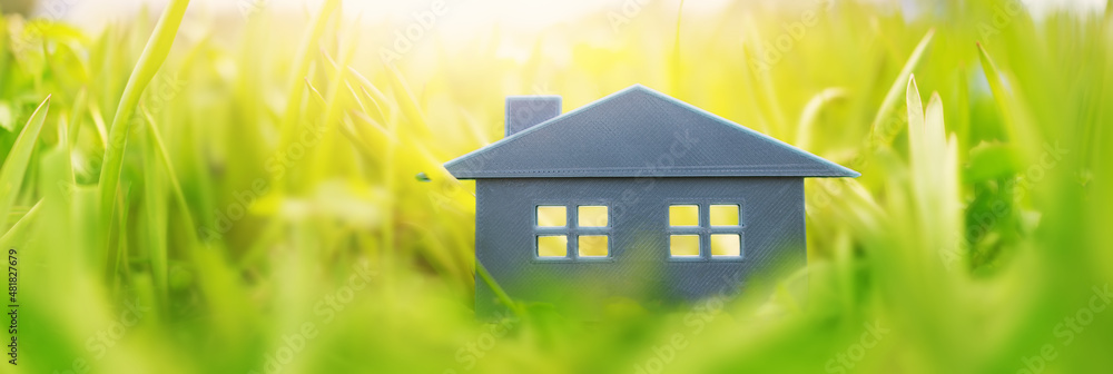 Grey plastic model of the house on the fresh grass on a sunny day.