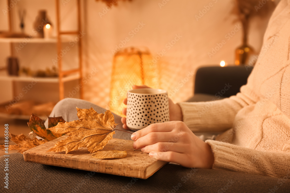 Woman with cup of coffee, book and autumn leaves at home